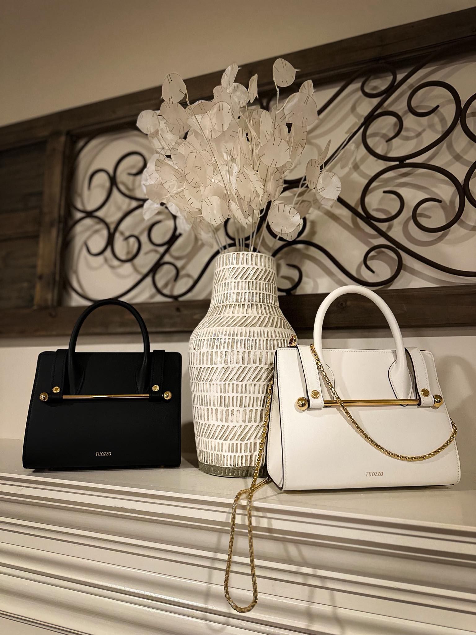Black and white handbags on a striped dresser with a tall decorative vase and floral arrangement