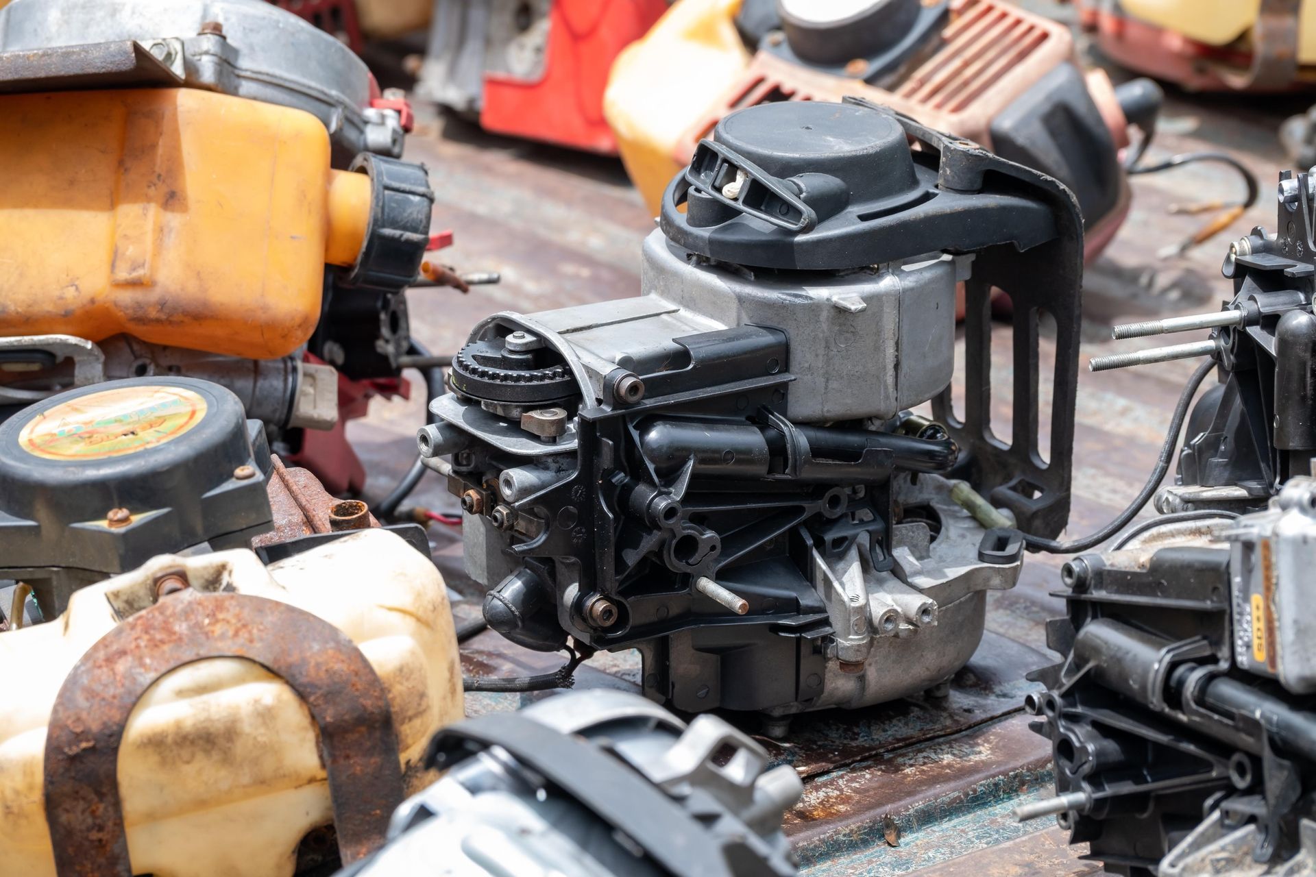 Pile of old, greasy small engines and mechanical parts on a workbench.