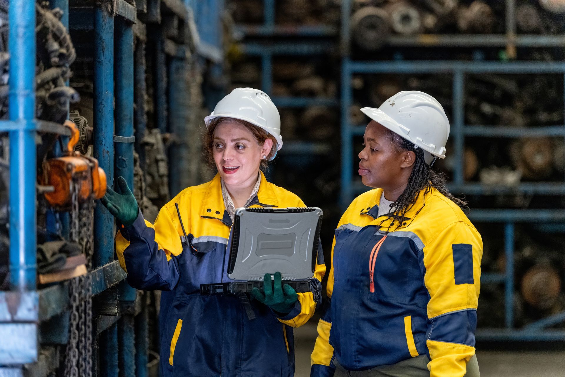 Technicians inspecting inventory of used automotive parts for sale in warehouse with tablet.
