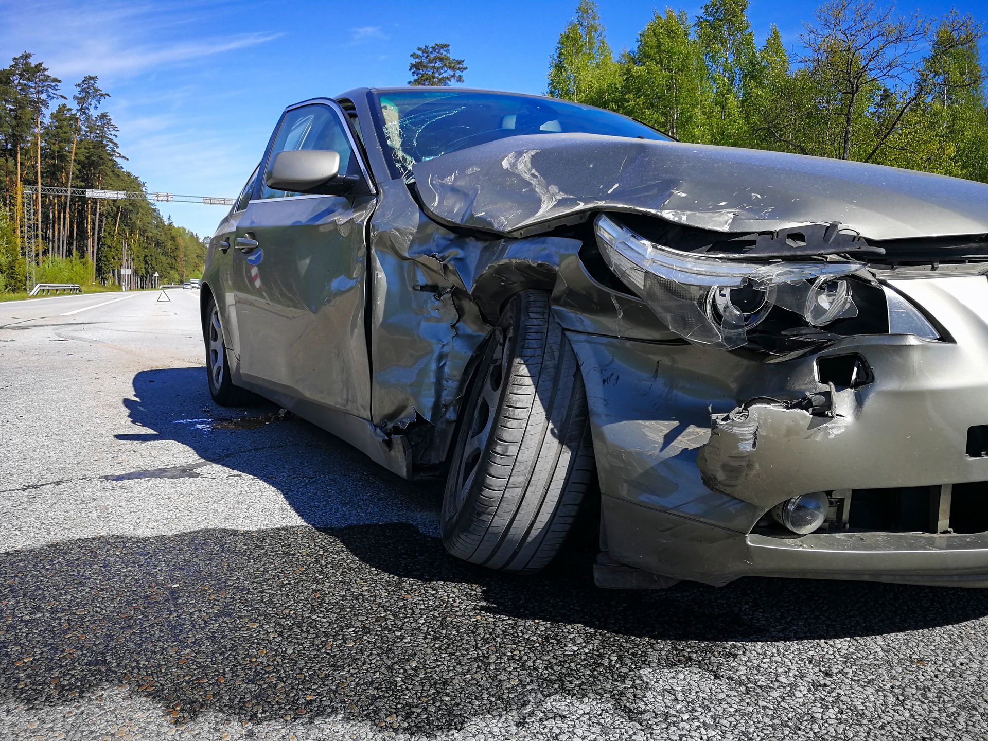 Crashed sedan with severe front-end body damage awaiting auto salvage buyers on the highway.