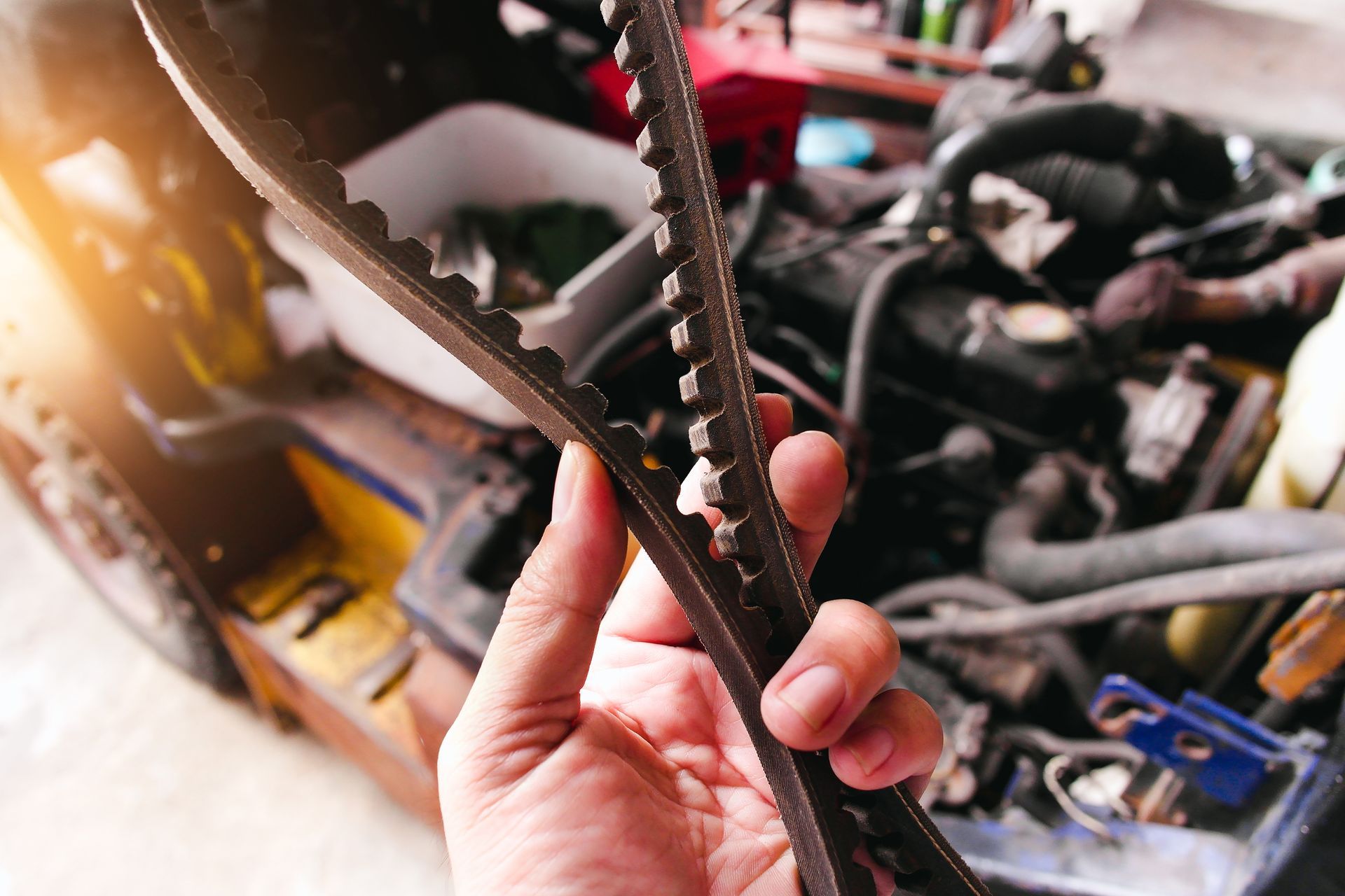 Hand holding a worn engine belt in front of an open vehicle engine.