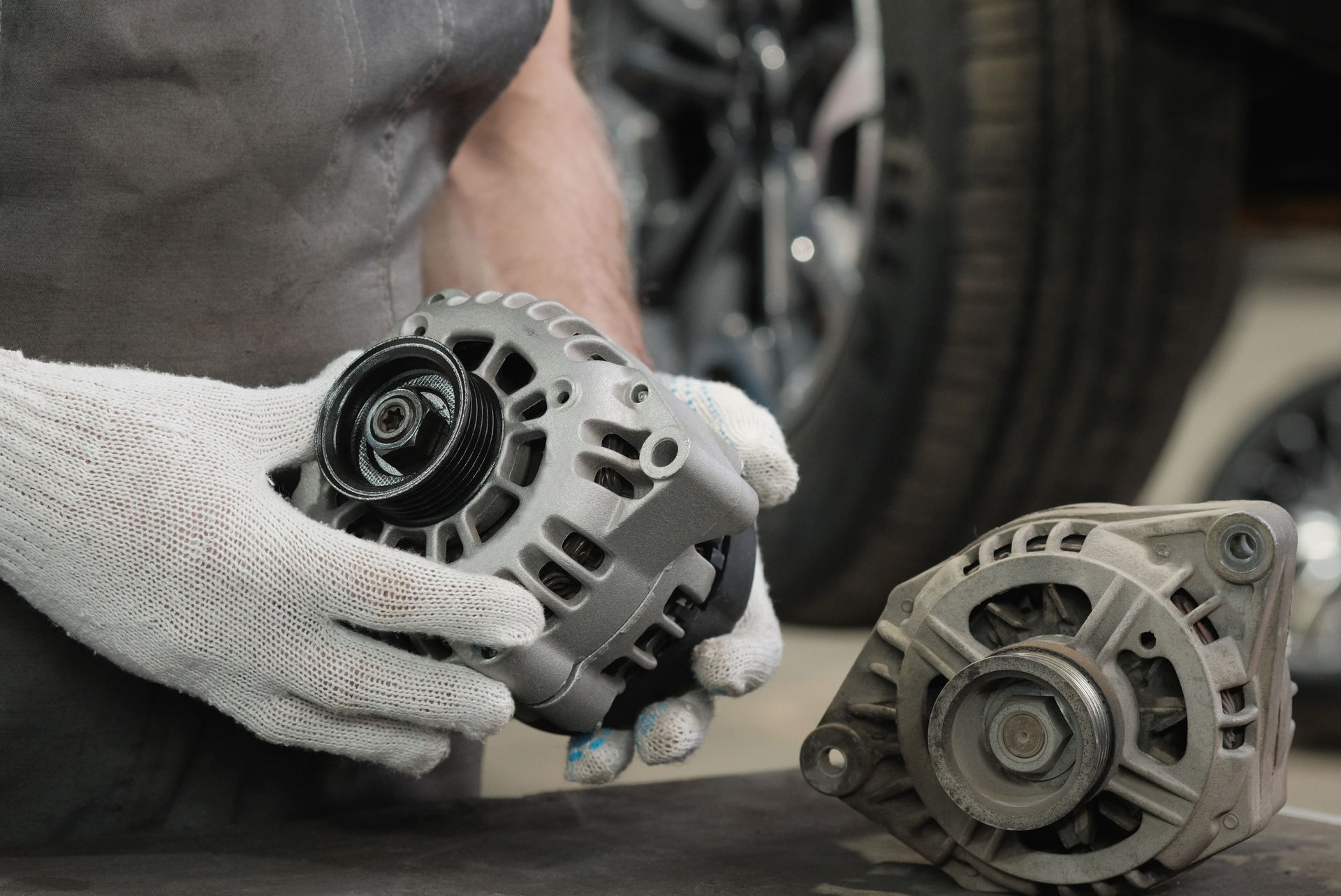 Gloved hands holding a new car alternator beside an old unit on a workbench