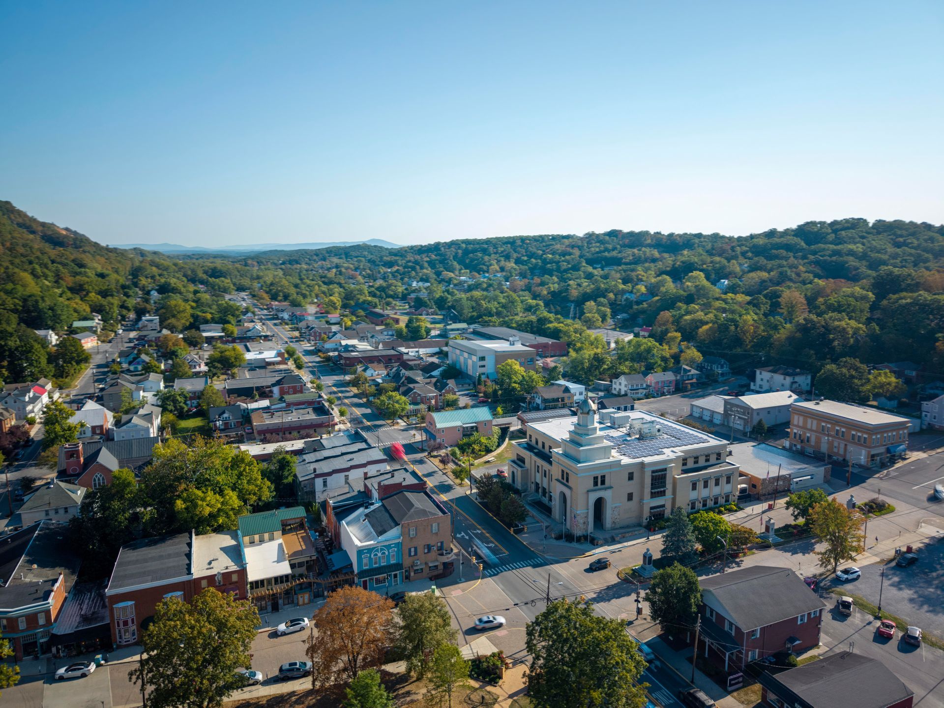 Aerial view of a small town with buildings, streets, and green hills under a clear blue sky