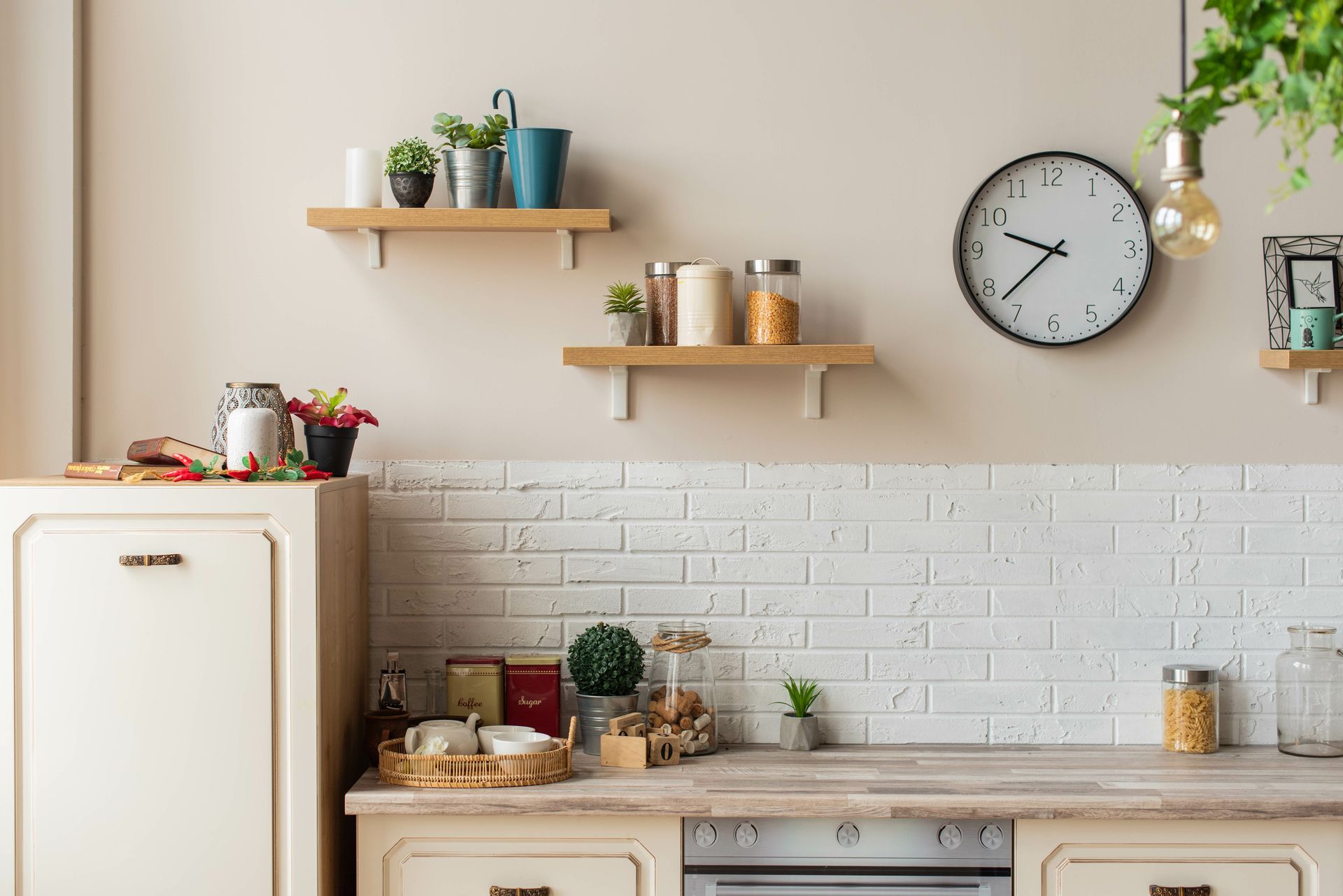 Bright kitchen with white cabinets, wooden shelves, potted plants, jars, and a wall clock