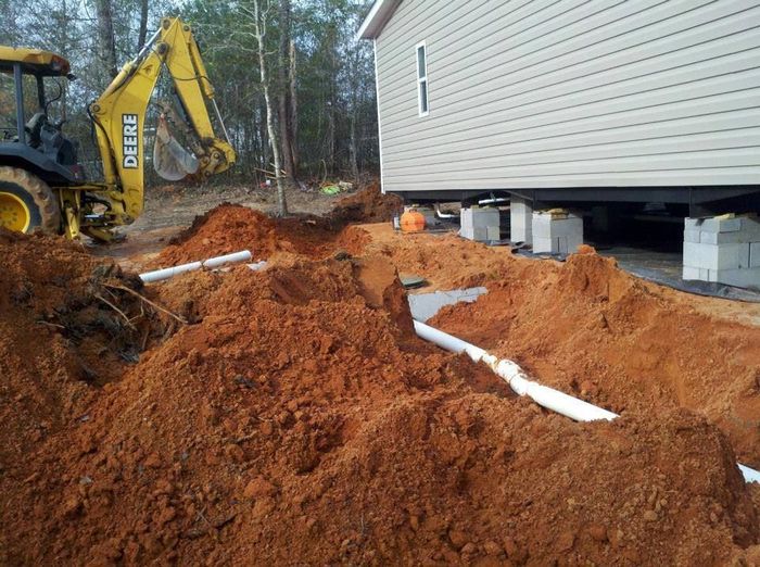 A yellow deere backhoe is digging a hole in front of a house