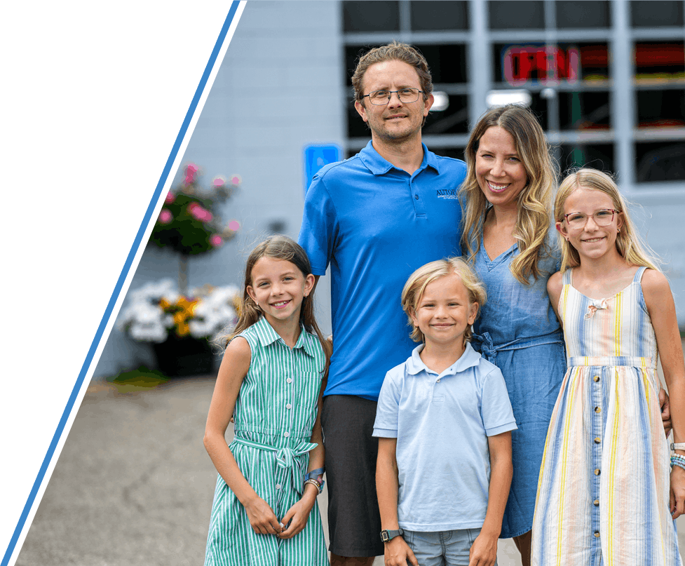 Family of four standing outdoors in front of the Autopia Bloomington shop, smiling at the camera.