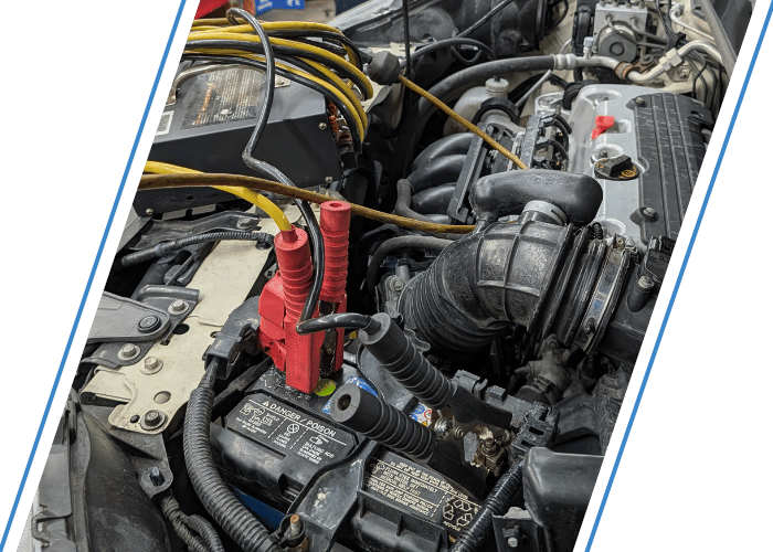 Engine bay with battery testing equipment connected during a battery inspection and charging service.