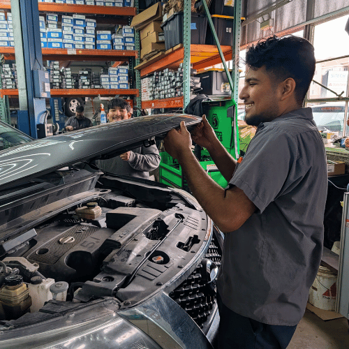 Mechanic inspecting a car engine in a garage, with shelves of parts in the background