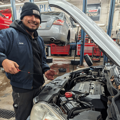 Mechanic smiling beside an open car hood in a busy auto repair shop