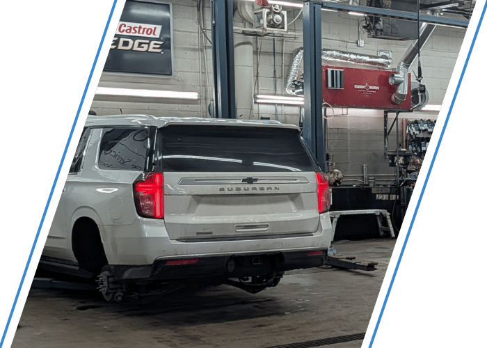 White Chevrolet Suburban positioned for suspension or brake repairs inside the shop.