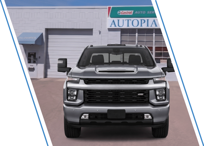 Front view of a silver Chevrolet heavy-duty pickup truck parked outside an auto repair shop.