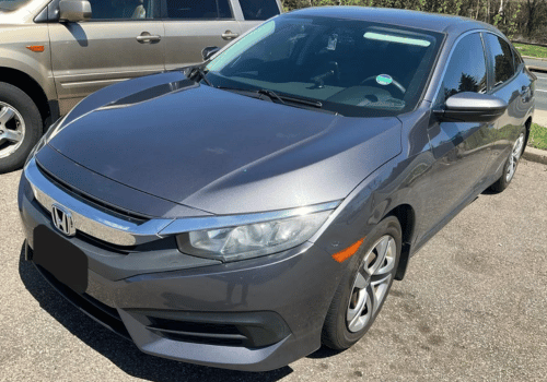 Gray Honda Civic sedan parked outdoors in a parking lot, shown from the front driver's side on a sunny day.