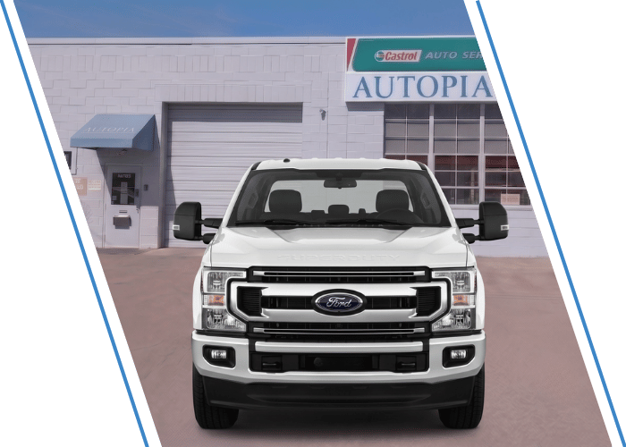 Front view of a white Ford Super Duty pickup truck parked outside an auto repair shop.