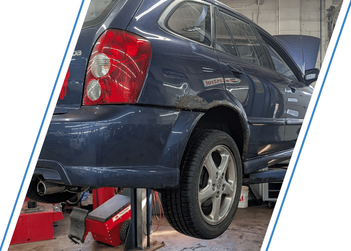 Blue SUV on a lift with visible rust damage during fuel system inspection and repair.