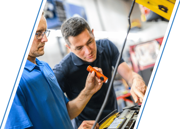Technician performing an undercar inspection with a flashlight while explaining findings.