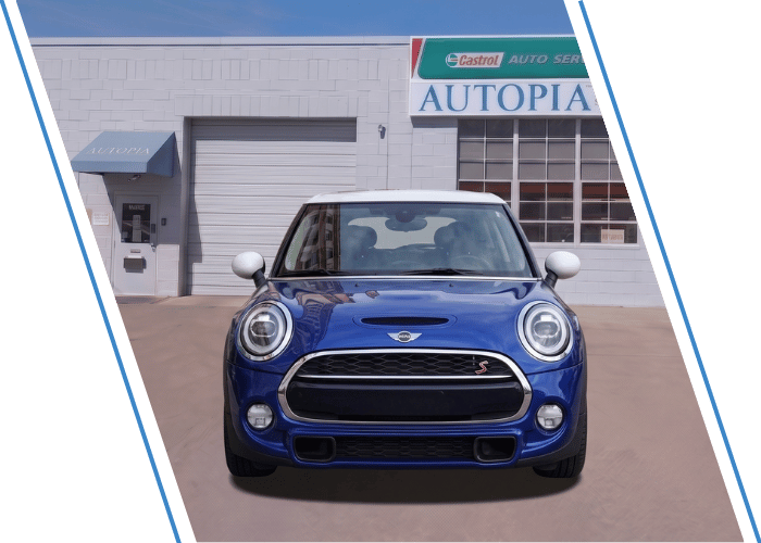 Front view of a blue MINI Cooper hatchback parked outside an auto repair shop.
