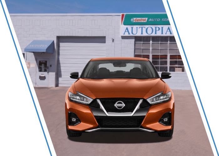 Front view of an orange Nissan sedan parked outside an auto repair shop.