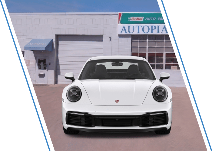 Front view of a white Porsche sports car parked outside an auto repair shop.