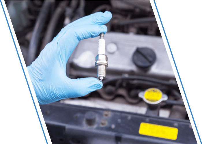 Mechanic holding a new spark plug in front of an engine compartment.