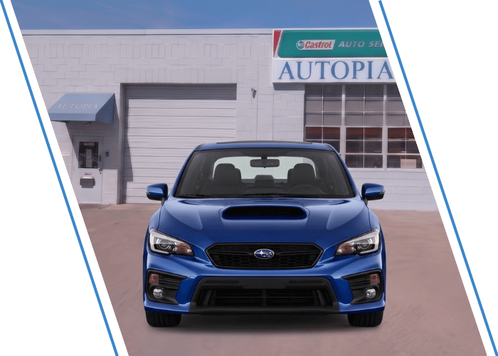 Front view of a blue Subaru sports sedan parked outside an auto repair shop.