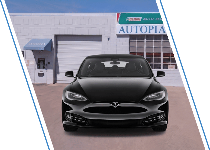 Front view of a black Tesla sedan parked outside an auto repair shop.