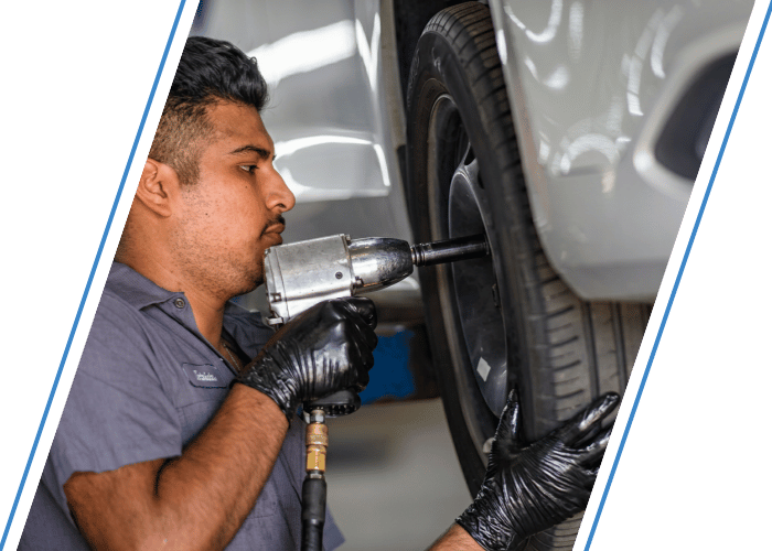 Technician using an impact wrench to remove a vehicle wheel during tire service.
