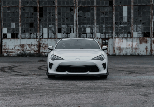 Front view of a white Toyota sports coupe parked in front of an industrial warehouse