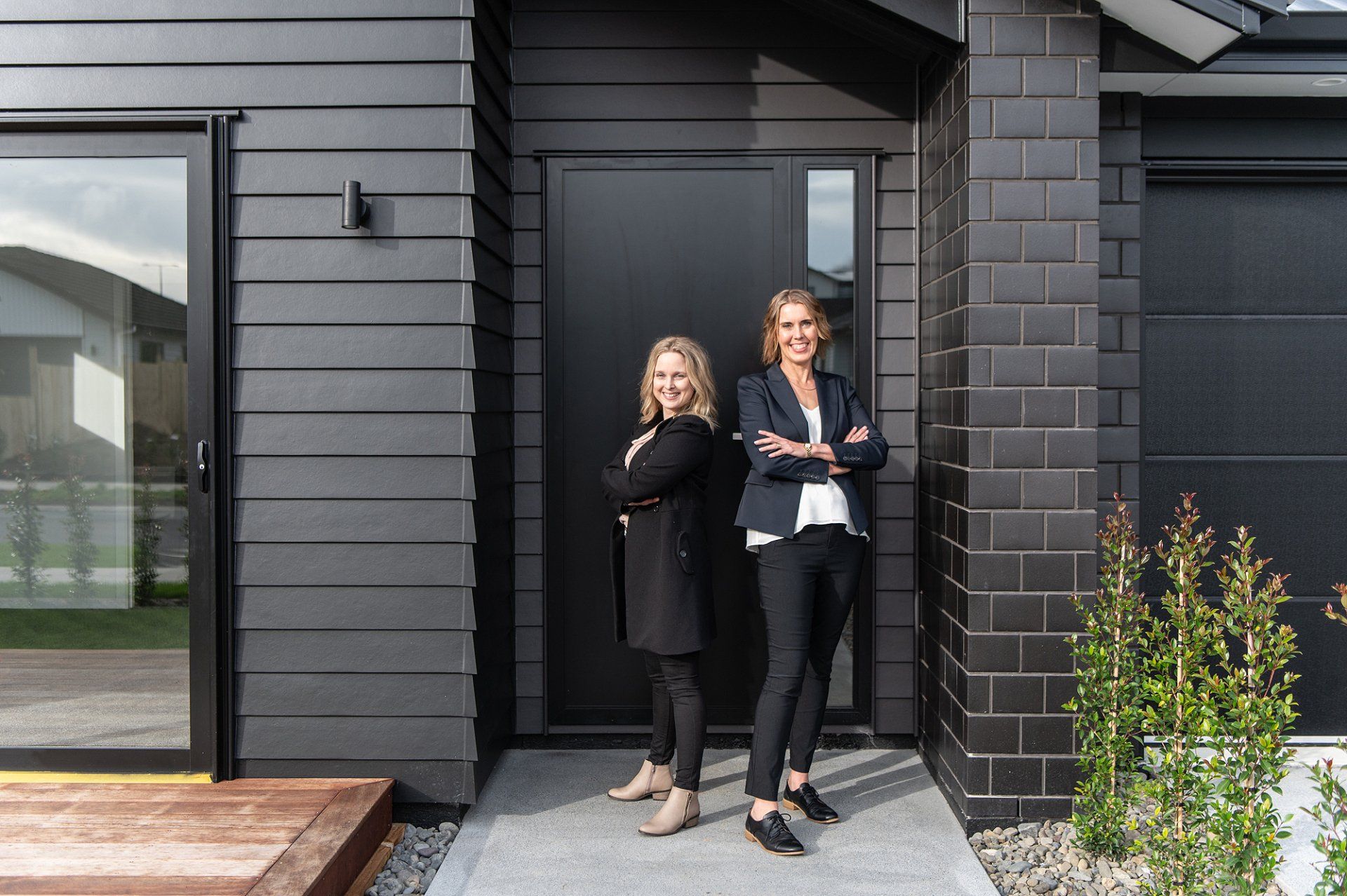 Vanessa and Lana standing at a modern black front door, holding papers and smiling