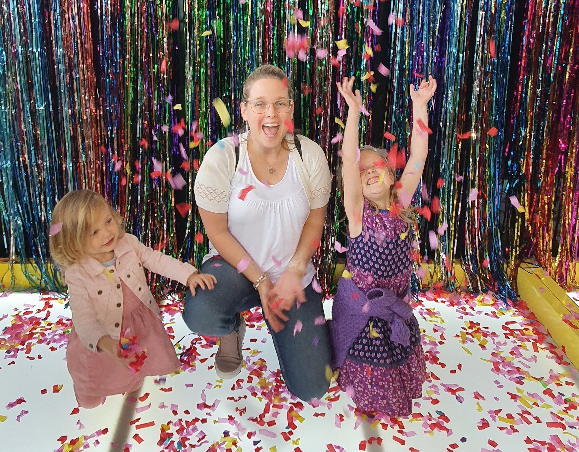 Lana kneeling with children and cheeringamid falling confetti in front of a colorful backdrop.