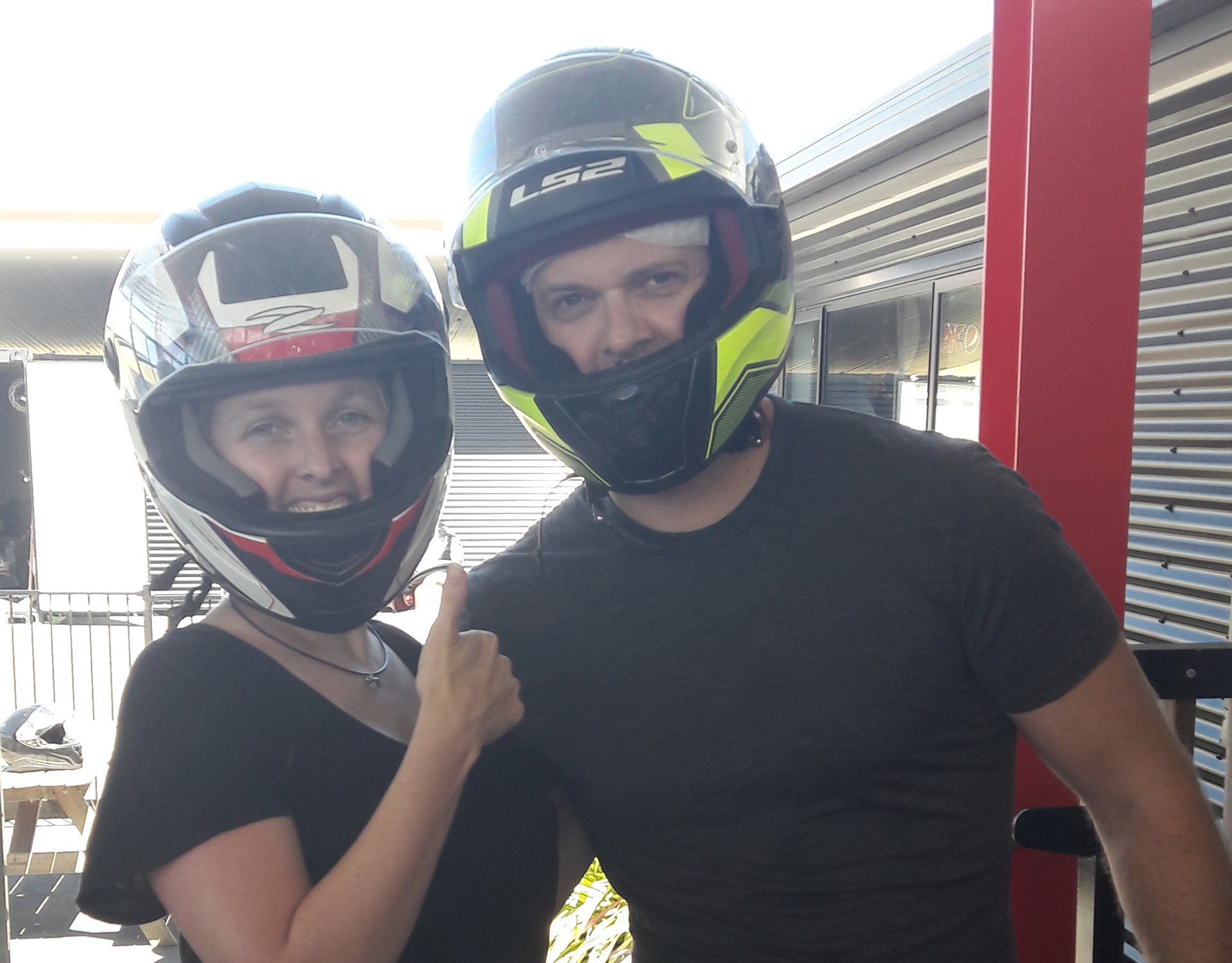 Lana and husband in helmets posing together, one pointing at the other, outdoors in bright sunlight.