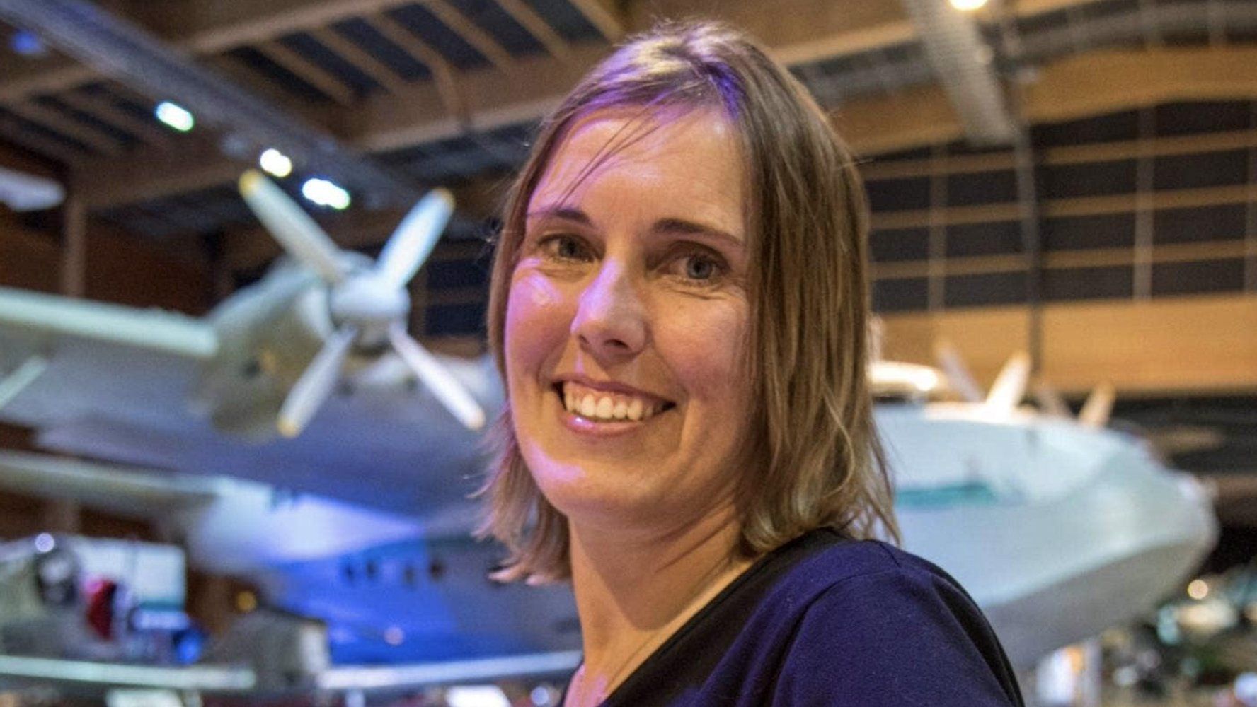 Vanessa - Smiling woman in a museum hangar with an aircraft in the background