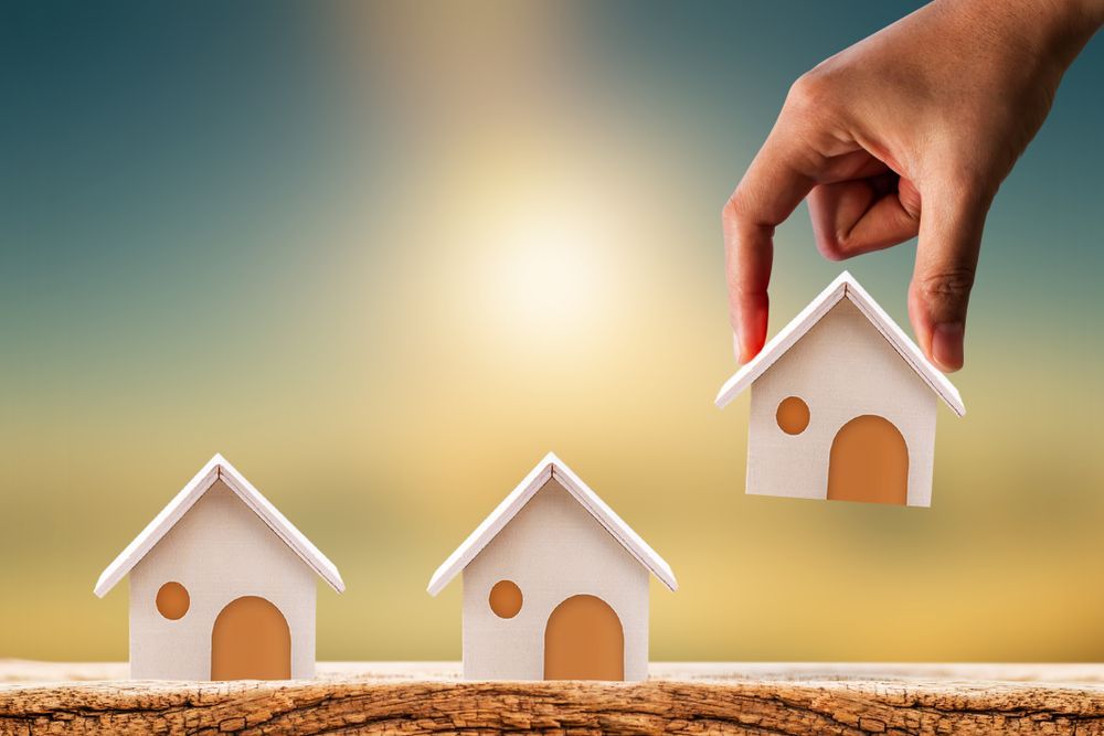A Hand Is Holding Three Small Houses in A Row — Hager Surveying In Kyogle, NSW