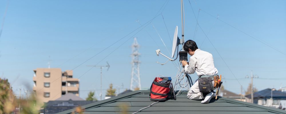 A Man Is Kneeling on Top of A Roof Working on A Satellite Dish — Hager Surveying In Palm Beach, QLD