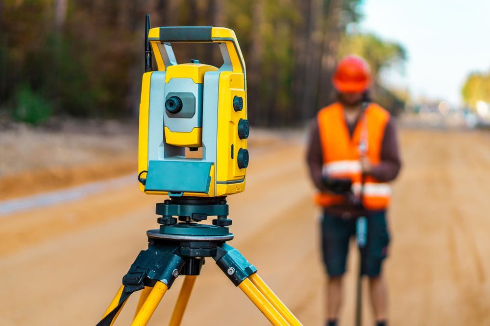 A Man Is Standing Next to A Yellow Theodolite on A Tripod — Hager Surveying In Gold Coast, QLD