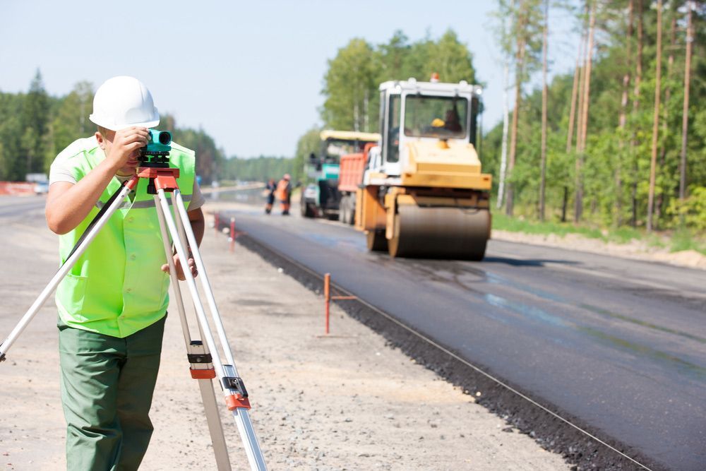 A Man Is Standing on A Tripod Taking a Picture of A Road Under Construction — Hager Surveying In Kingscliff, NSW