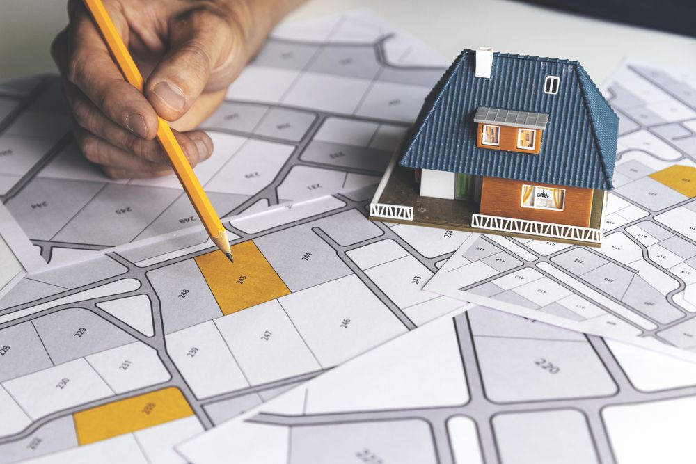 A Person Is Drawing a Map with A Pencil and A Model House on Top of It — Hager Surveying In Gold Coast, QLD
