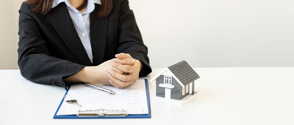 A Woman Is Sitting at A Table with A Clipboard and A Model House — Hager Surveying In Byron Bay, NSW