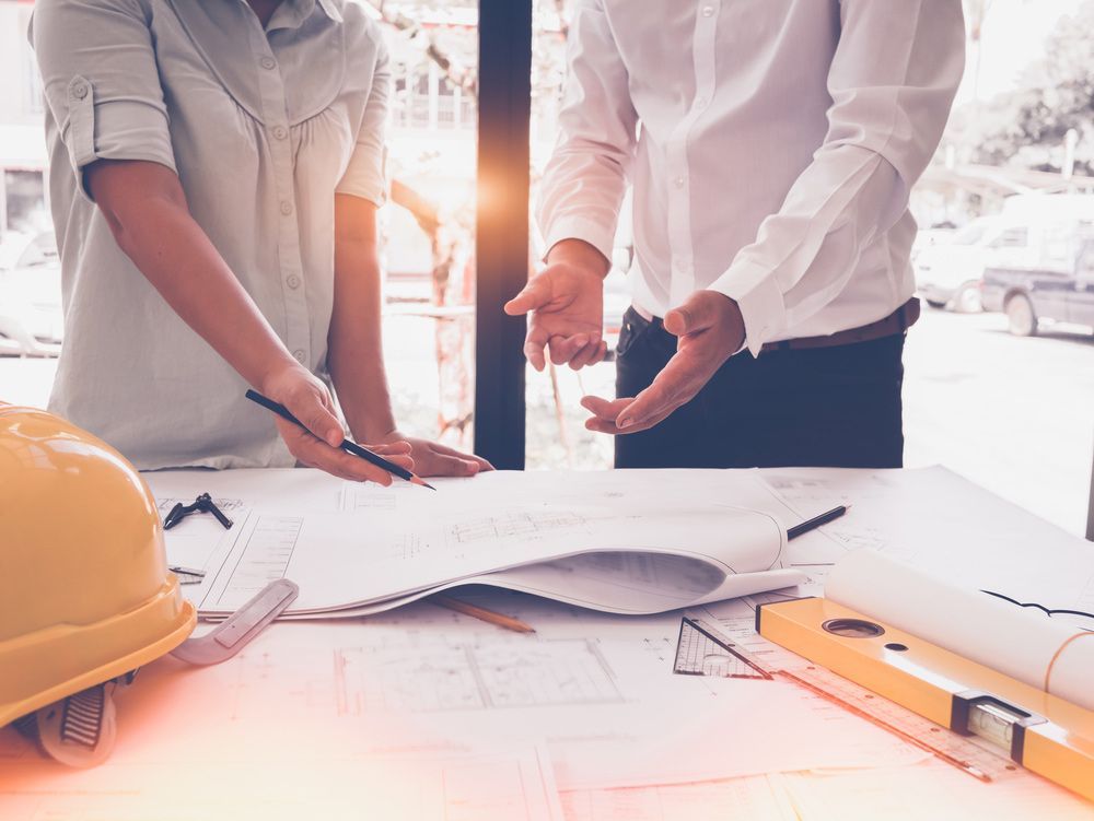 A Man and A Woman Are Looking at A Blueprint on A Table — Hager Surveying In Palm Beach, QLD