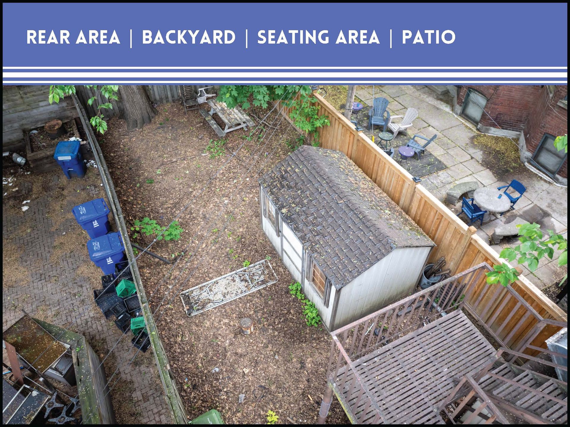 A backyard with a wooden shed, a metal fire escape, and a stone patio area with chairs on a sunny day.