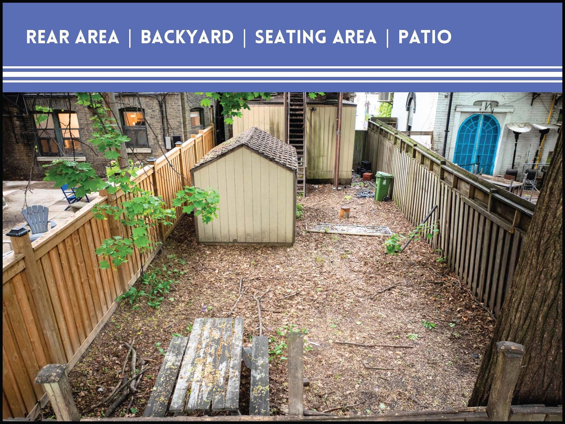 A backyard seating area features a beige shed, a wooden fence, a rustic picnic table, and a mulch-covered yard.