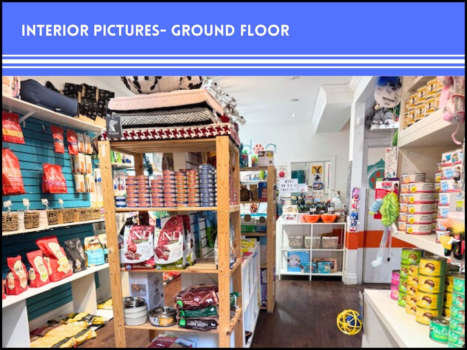 A pet supply store interior showing aisles filled with pet food bags, cans, and supplies on wooden and metal shelving.
