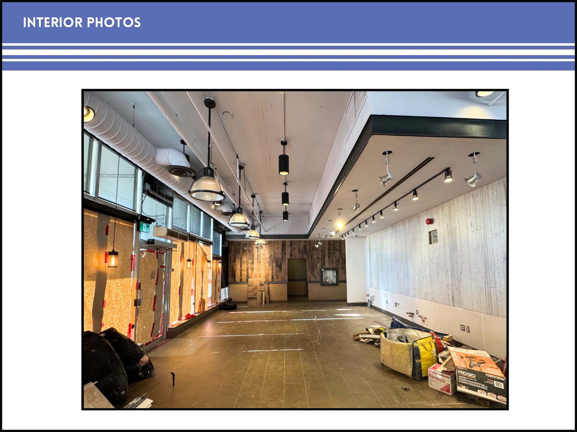 A wide-angle interior view of a vacant, rectangular commercial space with tile floors, pendant lights, and wall sconces.