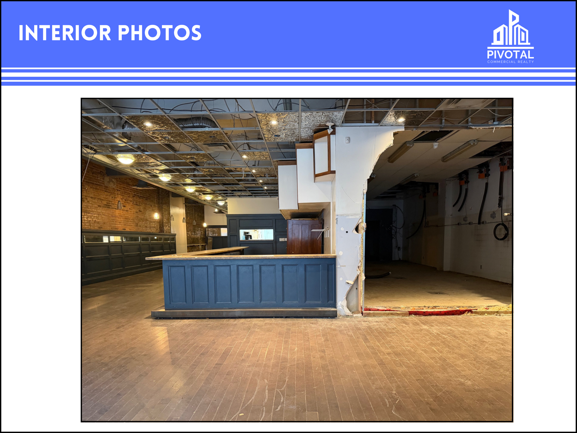 A renovation-in-progress commercial space featuring a blue bar counter, exposed ceiling, and wood flooring.