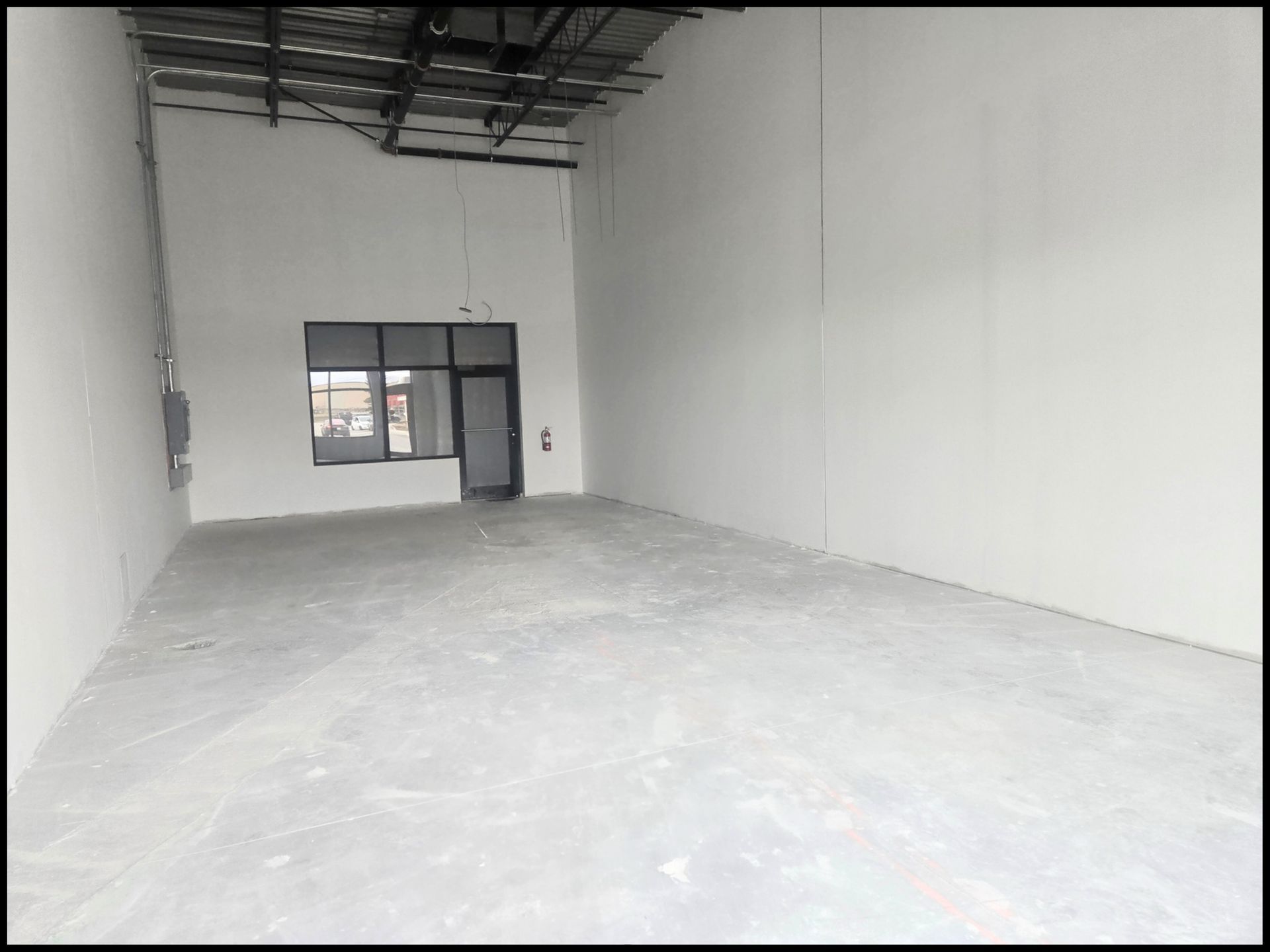 An empty warehouse or commercial space with white walls, a concrete floor, and an exposed ceiling structure.