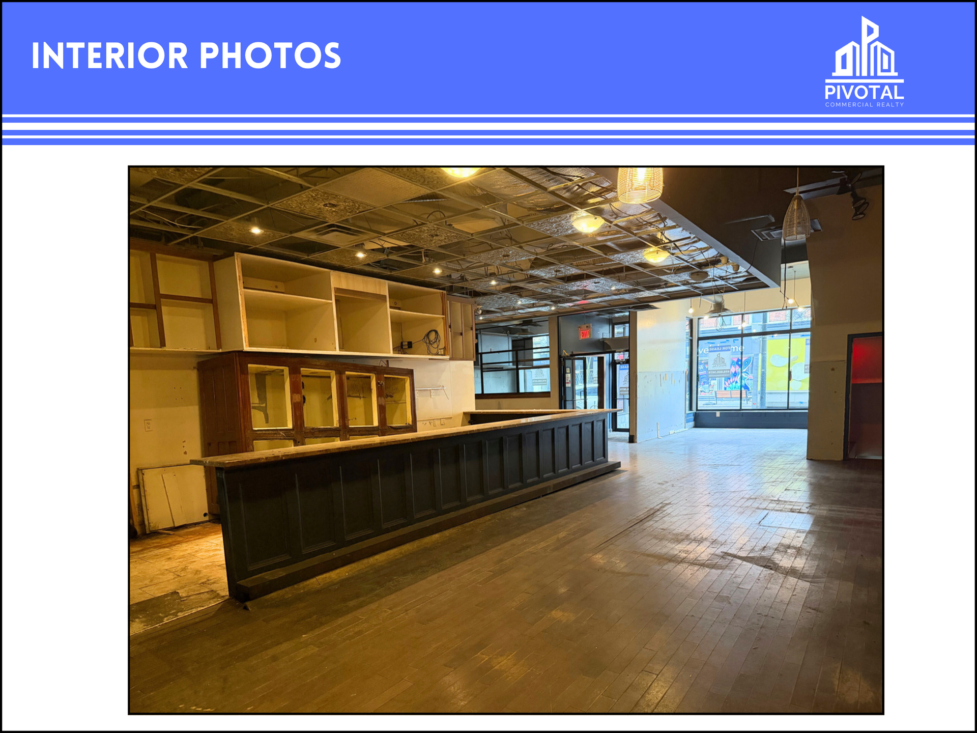 An interior view of a commercial space with a dark wood bar, white shelving, a decorative tin ceiling, and wood floors.