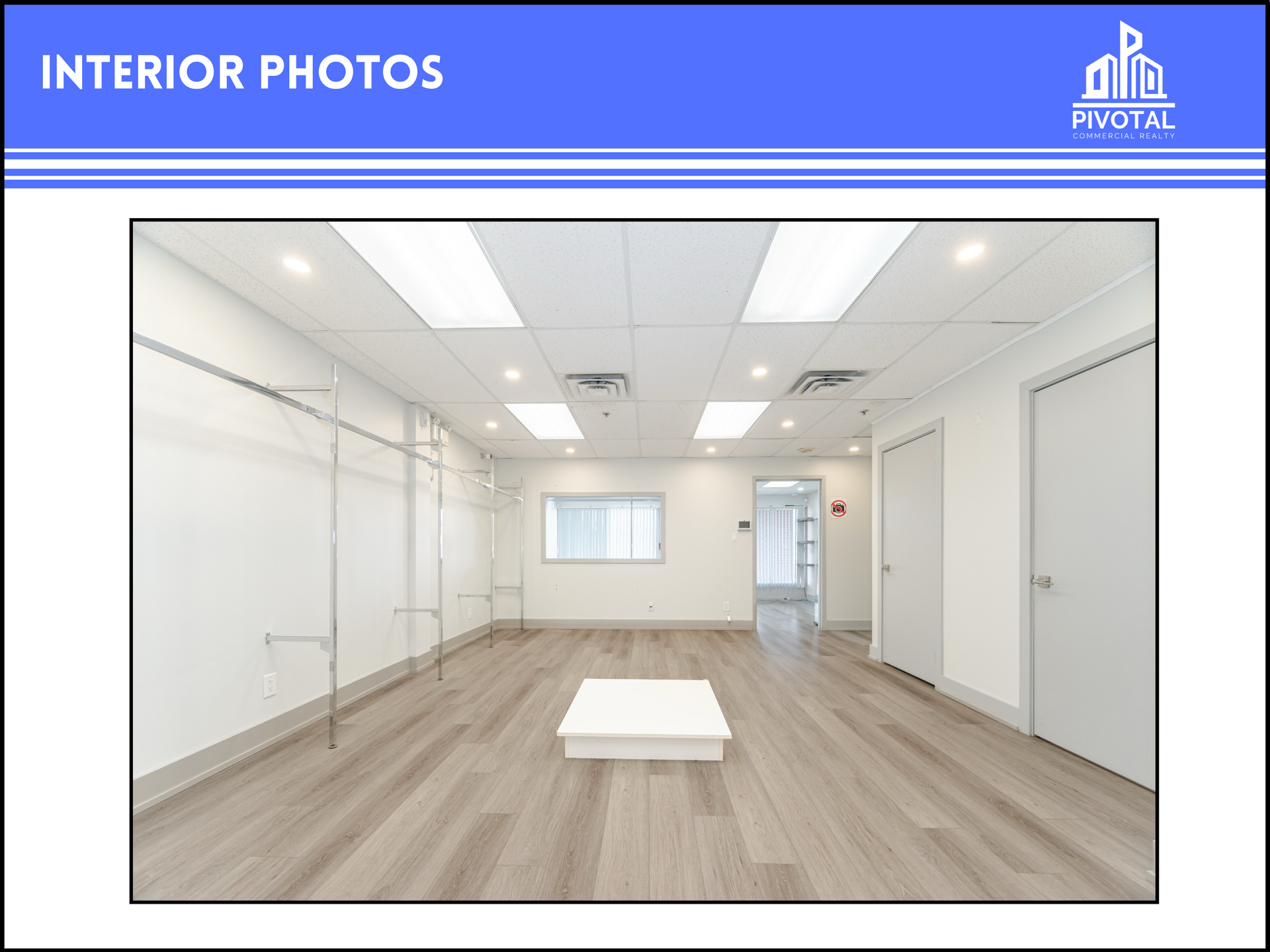 An empty, well-lit commercial space with white walls, light wood flooring, a drop ceiling, and wall-mounted garment racks.