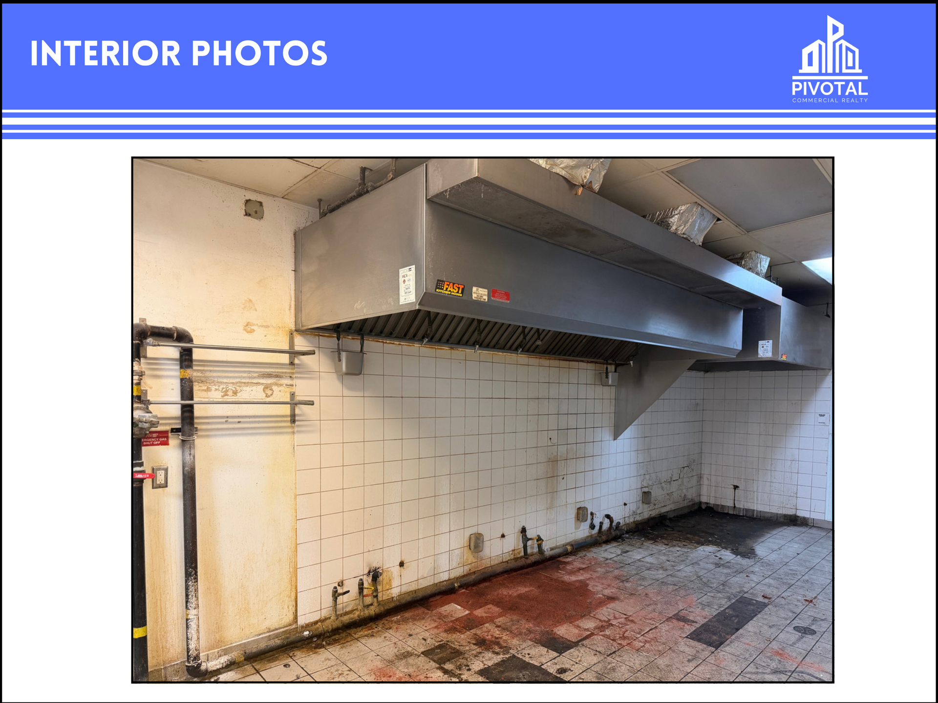 A commercial kitchen with a stainless steel vent hood over a tiled wall and floor, appearing vacant and in need of repair.