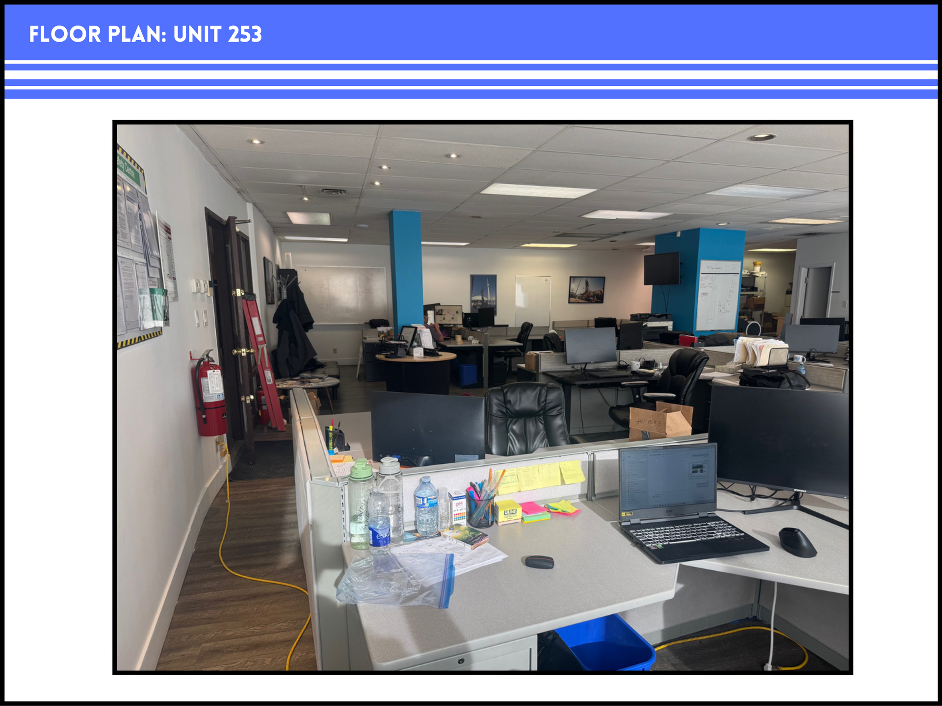 An open-plan office space, labeled Unit 253, featuring rows of cubicle desks, computer equipment, and blue structural pillars.