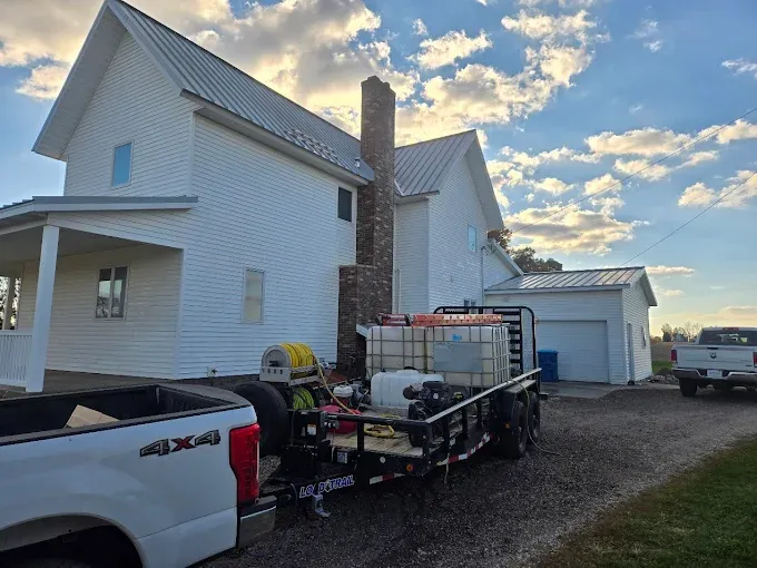 White house with trailer carrying tanks and equipment; blue sky, parked trucks.