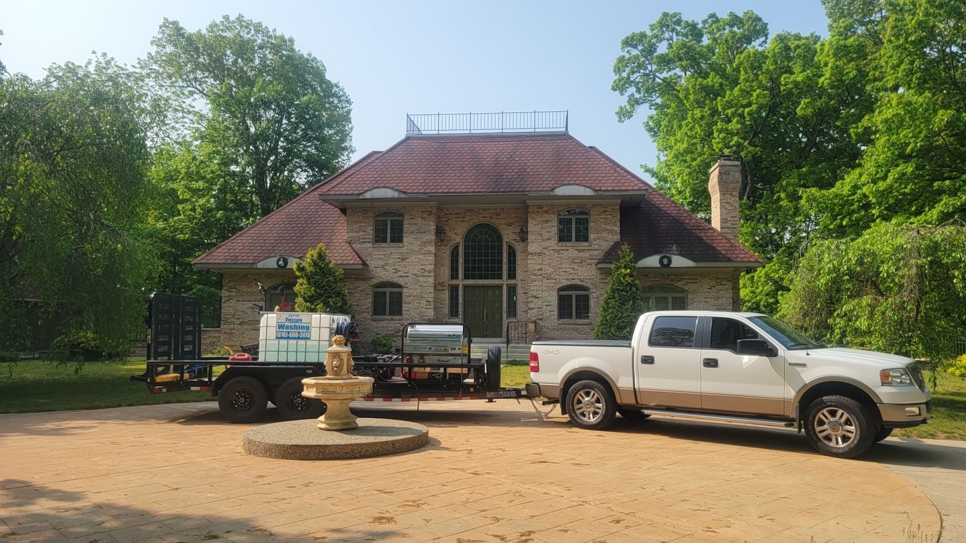 Tan brick house with red tile roof, truck, and trailer with equipment in front.